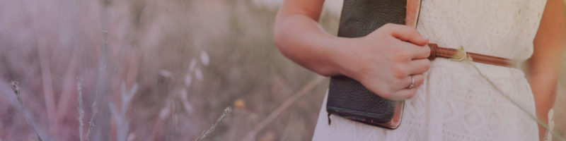 Woman holding Bible in field of wildflowers.